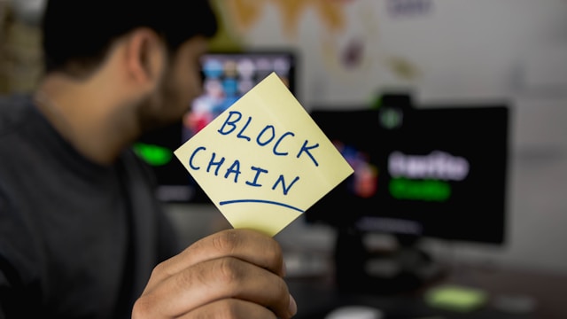 A person showing the word Blockchain written on a yellow sticker