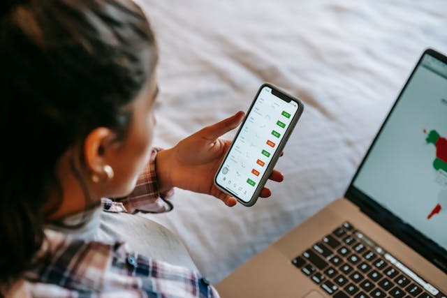 Crop ethnic analyst using trading application on smartphone on bed